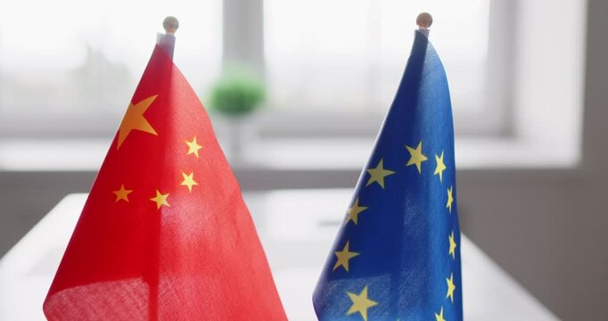 Flags show diplomacy, negotiation, bilateral dialogue, relations. China and European Union flags on a table suggest talks on trade and technology. Bilateral talks, policy focus stated.
