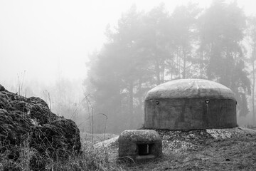 Stalowe pancerze starego bunkra w formie dzwon&oacute;w na tle mglistego lasu w czerni i bieli