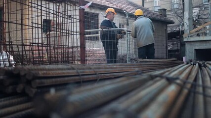 Construction workers are tying reinforcing mesh during building structure, rebar in the blurred foreground, low angle view.