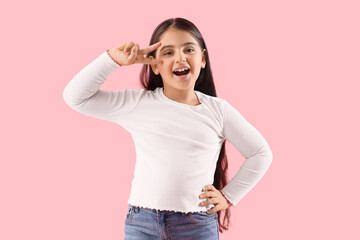 Little girl showing victory gesture on pink background