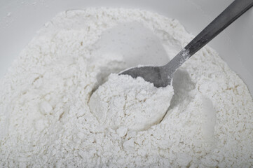 White flour in a bowl being mixed with a tablespoon, close-up