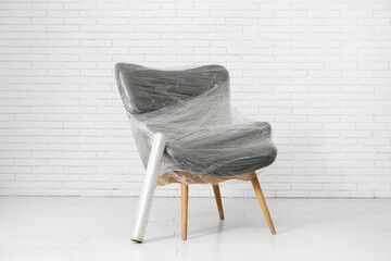 Wrapped armchair with stretch film near white brick wall in room on moving day