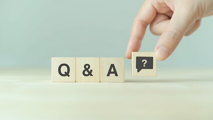 A close-up shot of a hand placing a question mark symbol on a cube that forms a part of the Q&A phrase, against a light backdrop of light colors. 