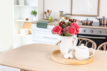 Vase with artificial flowers and teapot on dining table in kitchen