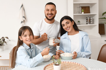 Happy family eating cottage cheese with cream at table in kitchen