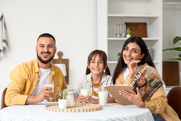 Happy parents and their little daughter with glasses of milk at table in kitchen