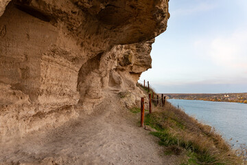 Scenic rocky trail carved along a cliff above a tranquil river, with open sky and distant landscape. Ideal for travel, adventure, and nature concepts.