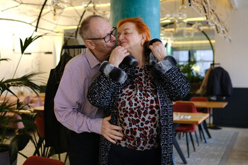 A man helps a woman put on her jacket and kisses her on the cheek. An adult couple, love, family, relationship, in a restaurant. High quality photo