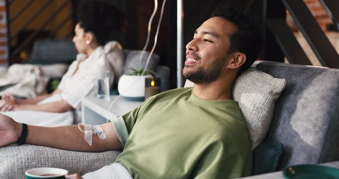 Man, happy and iv for drip therapy at lounge, coffee and thinking with saline solution for immune system. Person, smile and relax with needle, mineral infusion and tea with vitamin boost for benefits