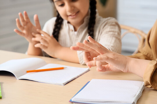 Mother with her little daughter using sign language while doing homework in kitchen, closeup