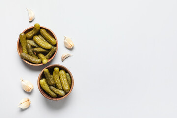 Wooden bowls with tasty pickled cucumbers and garlic on grey background