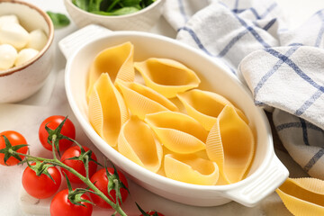 Baking dish with raw conchiglie pasta and tomatoes on light background