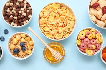Bowls with different cereals and ingredients on blue background, closeup