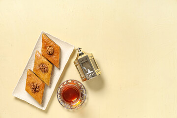 Fototapeta premium Glass of tasty Turkish tea with baklava and fanoos on beige grunge background. Ramadan celebration