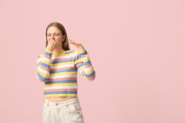 Young woman feeling disgusting smell on pink background