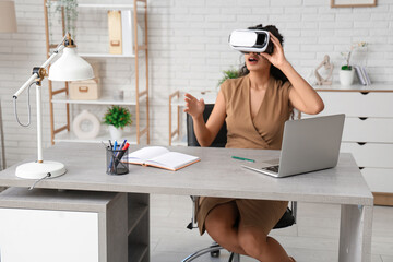 Young African-American businesswoman in VR glasses at table in office