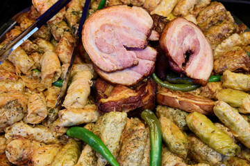 Pork knuckle on the grill and stuffed cabbage rolls prepared on grill at a Christmas market where various traditional dishes are served.