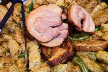 Pork knuckle on the grill and stuffed cabbage rolls prepared on grill at a Christmas market where various traditional dishes are served.
