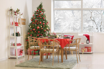 Stylish interior of festive living room with Christmas tree and served dining table