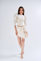 Young beautiful bride in a chic white outfit stands gracefully, embracing a moment of bliss