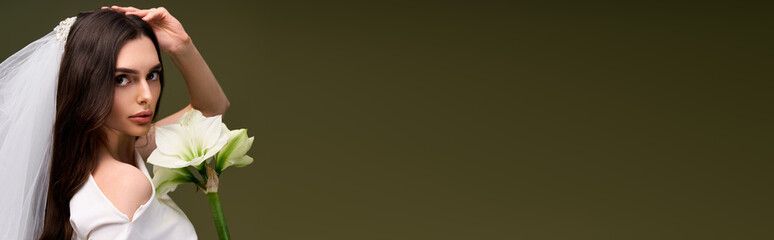 Young beautiful bride holding a white lily, radiating joy in a soft green backdrop