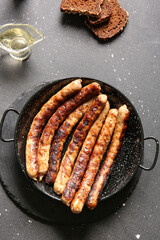 Frying pan of tasty grilled sausages on black background