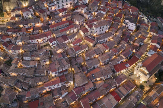 Aerial view of terracotta rooftops cascade down the hillside, illuminated by soft golden light, creating a warm, inviting glow over the ancient town, Rocca Imperiale, Calabria, Italy.