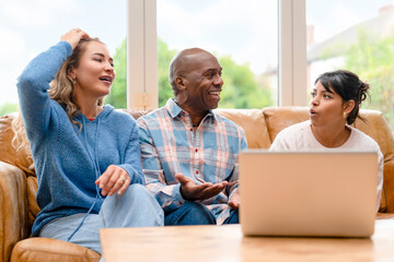 Friends share stories and laughter in a living room with a laptop during a casual afternoon