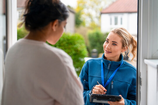 Woman talks with another woman at the door while holding a tablet in a residential area during daytime
