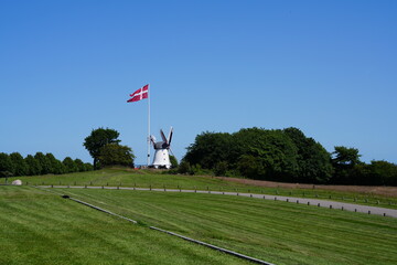 Fototapeta premium Düppeler Mühle, Dybbøl Mølle, Windmühle, Mühle, Holländerwindmühle, Düppeler Schanzen, Denkmal, Krieg, dänisch, deutsch, 1864, patriotisch, Sonderburg, Sonderborg, Dänemark, Himmel, blau, Fahne, Wiese
