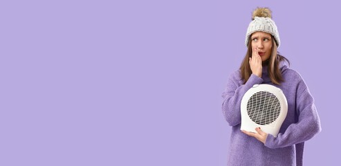 Frozen young woman in hat and with electric fan heater on lilac background with space for text