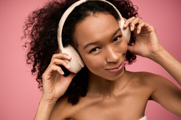 Obraz premium Joyful young woman enjoying music with stylish headphones against a vibrant pink backdrop