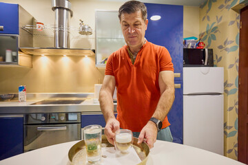 A middle-aged man at home in the morning makes coffee and serves it.