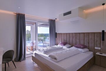 Fototapeta premium Bright, modern bedroom featuring a comfortable bed, sleek desk, and a large sliding glass door opening to a private balcony with stunning green landscape views, perfect for relaxation and serene