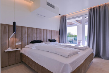 Fototapeta premium Bright, modern bedroom featuring a comfortable bed, sleek desk, and a large sliding glass door opening to a private balcony with stunning green landscape views, perfect for relaxation and serene