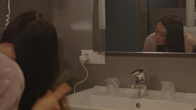 Overshoulder of an attractive Asian woman brushing her hair while standing in a hotel bathroom
