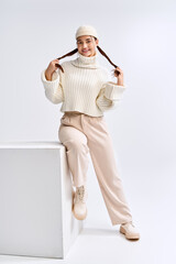 Charming teenage girl models cozy winter style in bright white studio