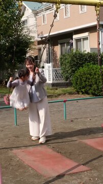 Happy Japanese mother pushing her little daughter on a swing at a playground in Japan