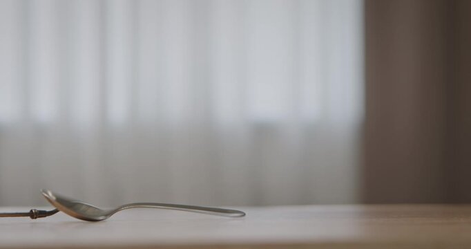 Metal teaspoons falling onto the surface of a wooden table in soft natural light indoors, minimalist composition