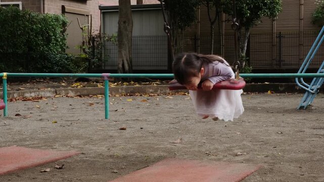 Young girl swinging back and forth in a Japanese park playground