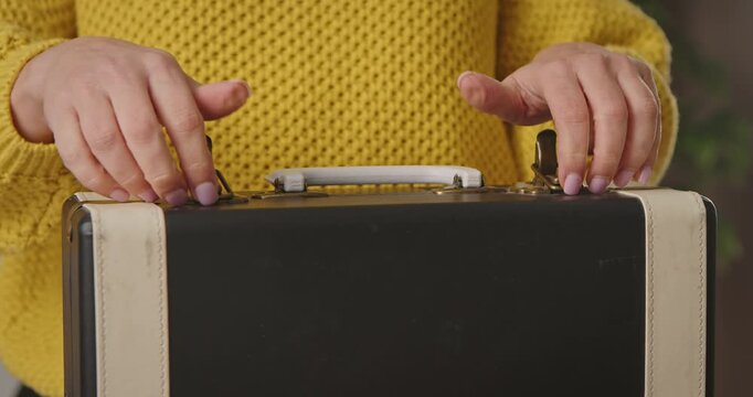 A woman in a yellow sweater opens and closes a vintage retro suitcase, close-up of hands and an old travel suitcase.
