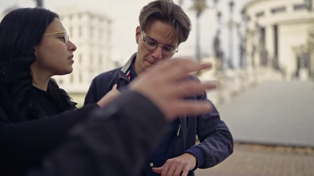 A group of young friends is deeply engaged, using a digital tablet to discuss and plan their next steps while exploring a vibrant urban environment outdoors.