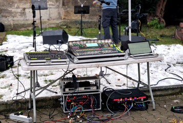 Next to the main console is a smaller analog mixer for submixing. An open laptop for controlling  digital console or playing music. Microphones, speakers and speakers in stands for outdoor production