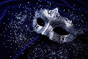 Silver ornate masquerade mask with glitter on dark blue velvet cloth. Mystical carnival design for party invitation or elegant event decor.