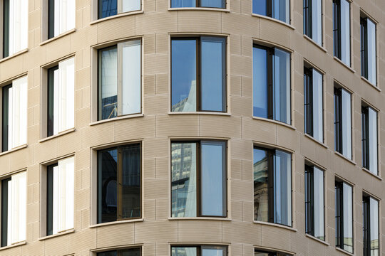 View of the building's facade features symmetrical rows of dark-framed windows reflecting the sky, set against the stone walls, Frankfurt am Main, Hessen, Germany.