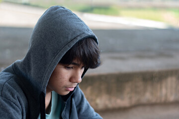 A quiet, melancholic moment. A middle school teenagd boy, wearing a grey hooded sweatshirt, sits alone with a sad, introspective expression. Capturing feelings of solitude and youthful contemplation