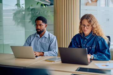 Diverse business colleagues focusing on tasks using laptops in a contemporary corporate office environment during a work session