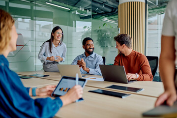 Diverse business professionals sharing ideas, smiling, and using technology during a productive meeting in a modern office environment