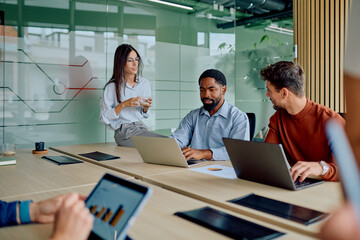 Professionals working on laptops and tablets, discussing strategy and analyzing data in a modern corporate boardroom