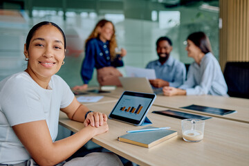 Confident businesswoman smiling at camera with diverse colleagues collaborating and discussing data in a corporate conference room